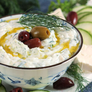 Tzatziki Sauce in a blue and white bowl with kalamata olives on top and olive oil drizzles around it.