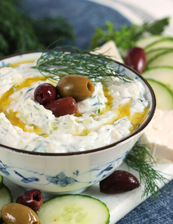 Tzatziki Sauce in a blue and white bowl with kalamata olives on top and olive oil drizzles around it.