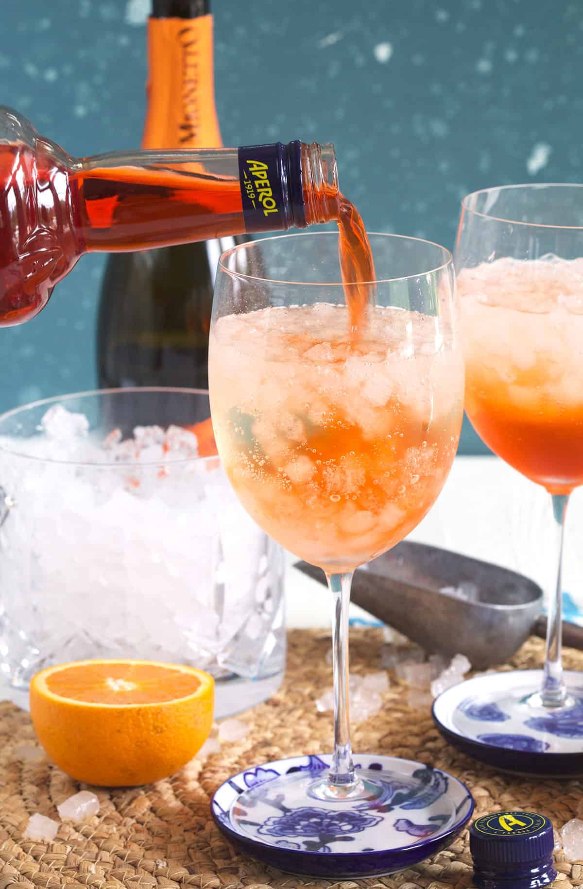 Aperol is being poured into a glass filled with ice and prosecco. 