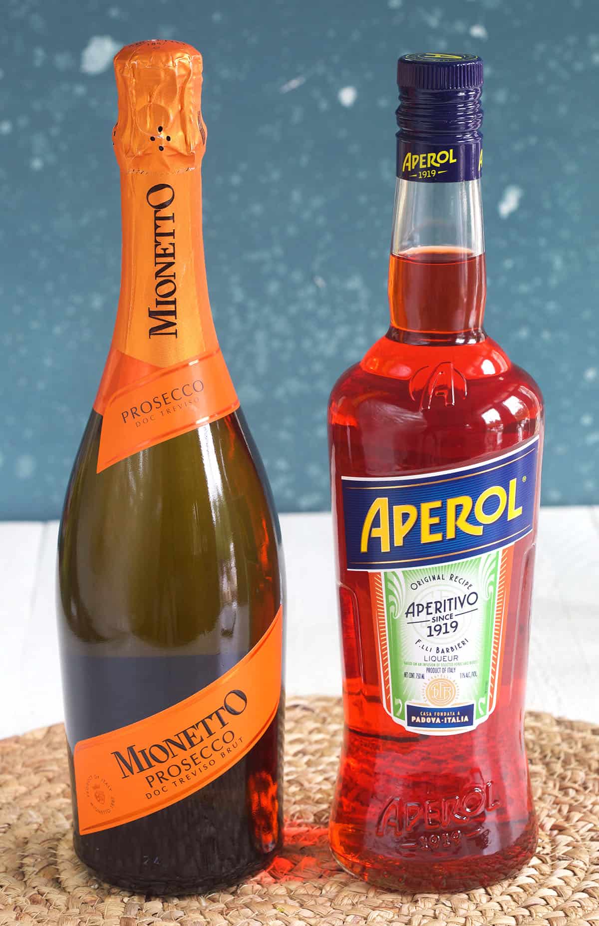 A bottle of prosecco is placed next to a bottle of aperol. 