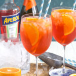 An aperol spritz is garnished with an orange slice and two straws.