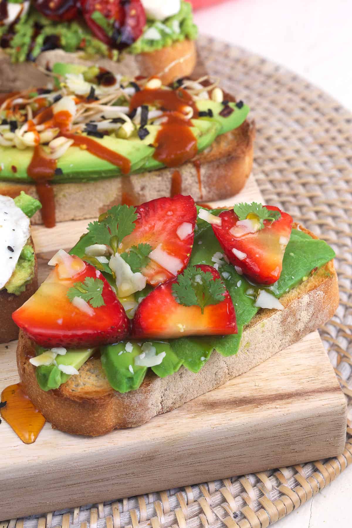 A piece of avocado toast is topped with fresh strawberries. 
