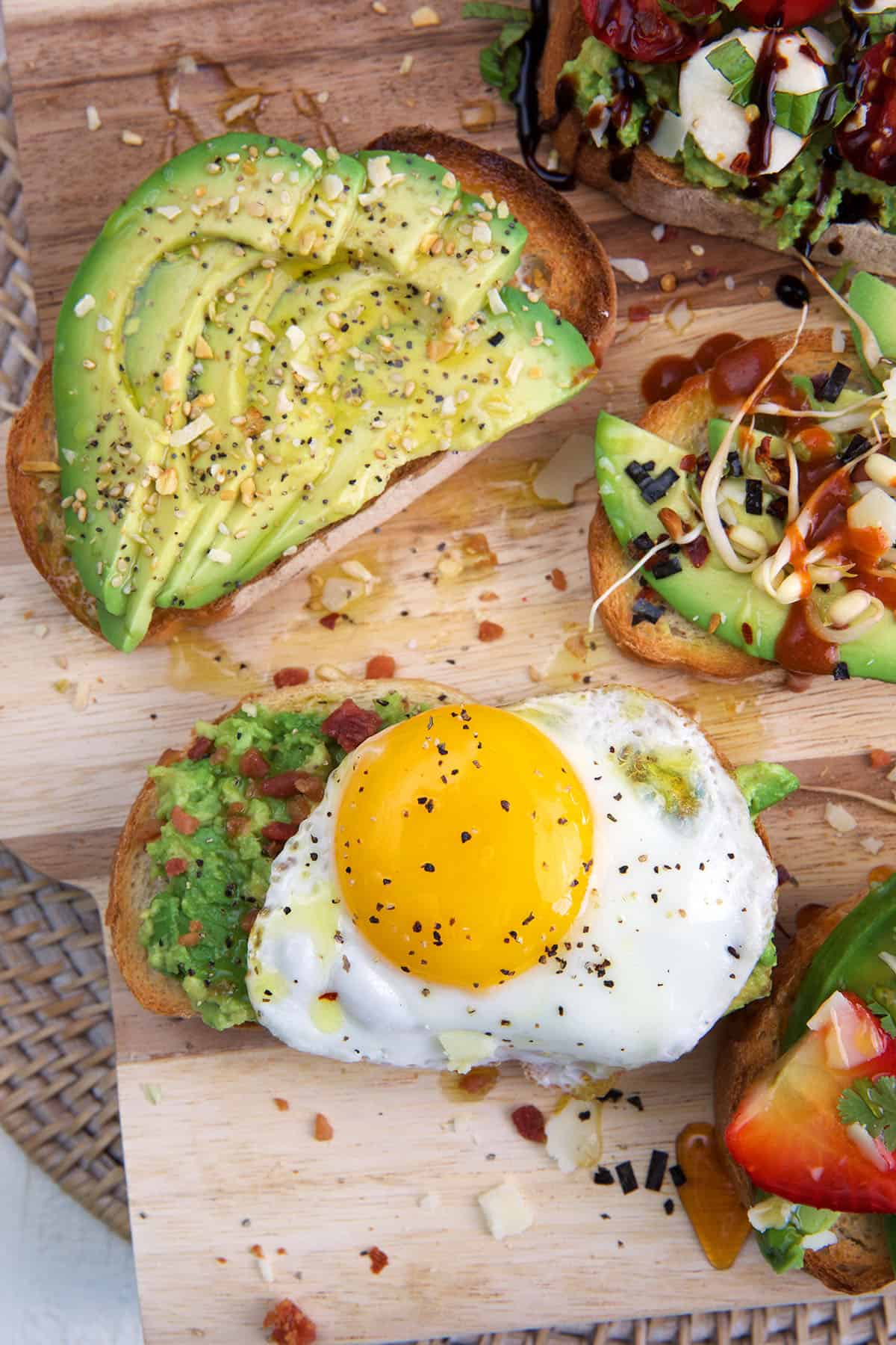 Two pieces of avocado toast are placed on a wooden cutting board. 