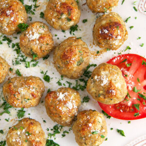 A slice of tomato is placed next to a batch of cooked meatballs.
