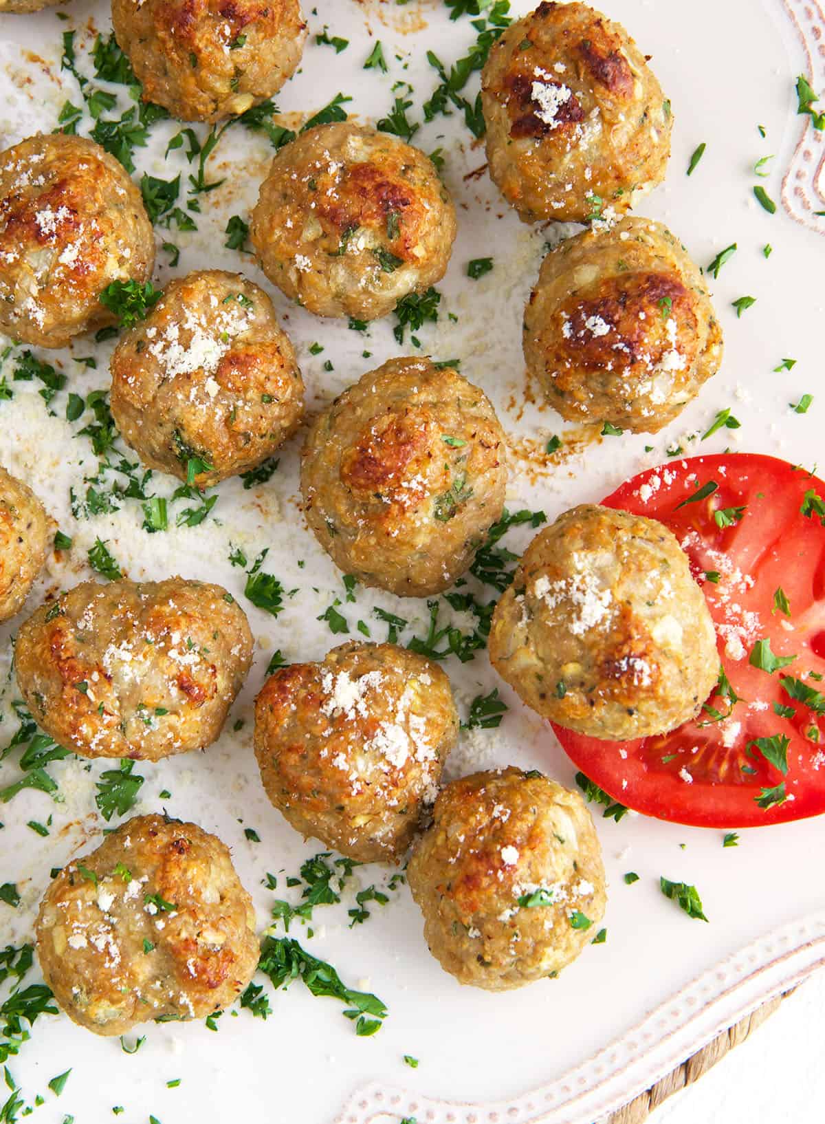 A slice of tomato is placed next to a batch of cooked meatballs. 