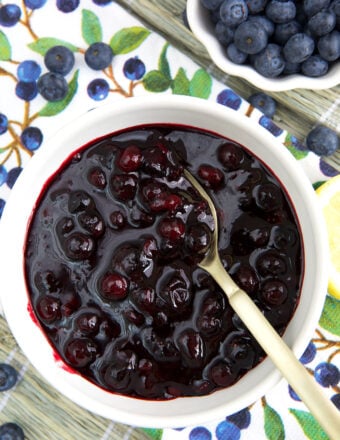 A white bowl is filled with blueberry compote and a spoon.