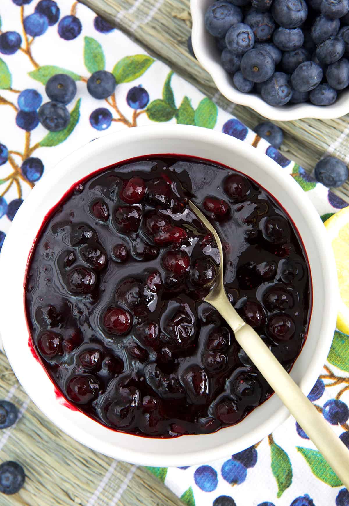 A white bowl is filled with blueberry compote and a spoon. 