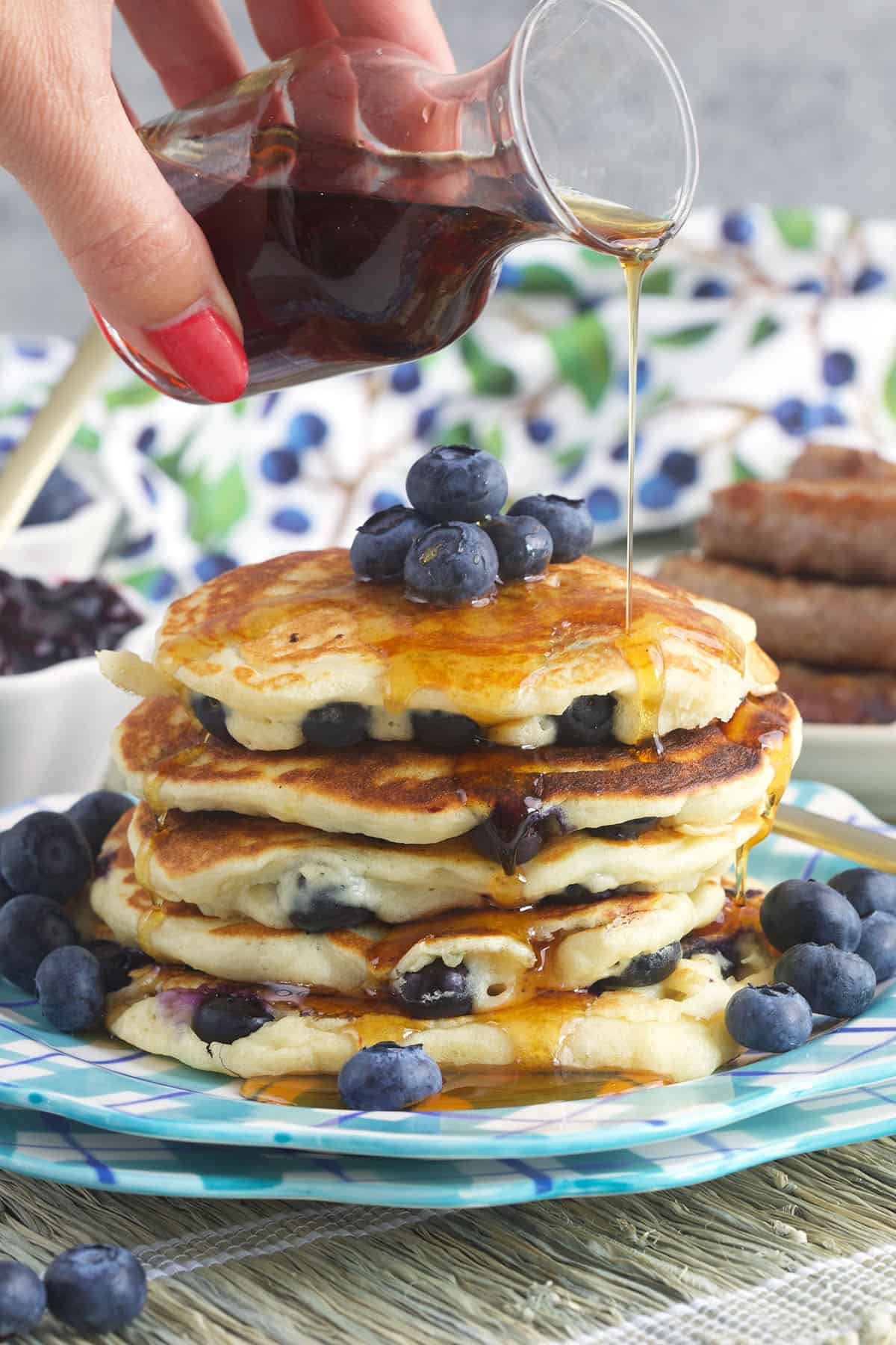 Syrup is being drizzled on top of a stack of blueberry pancakes. 