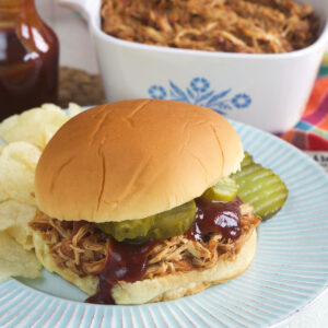 A bbq chicken sandwich is plated with potato chips.