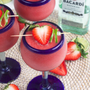 Several daiquiris are garnished with strawberries and limes.