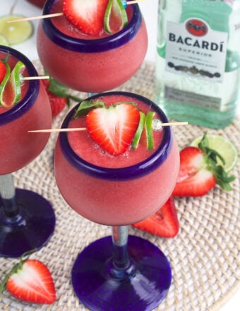 Several daiquiris are garnished with strawberries and limes.