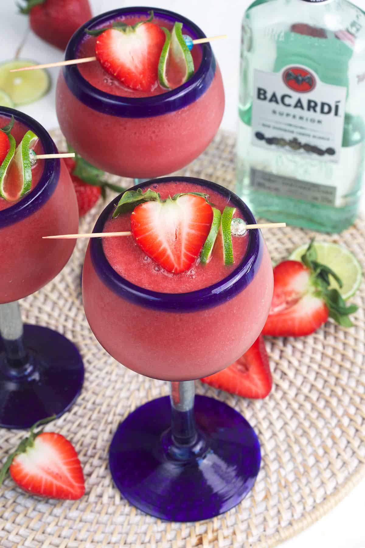 Several daiquiris are garnished with strawberries and limes. 