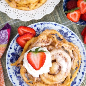 A strawberry is placed on some whipped cream atop a single funnel cake.