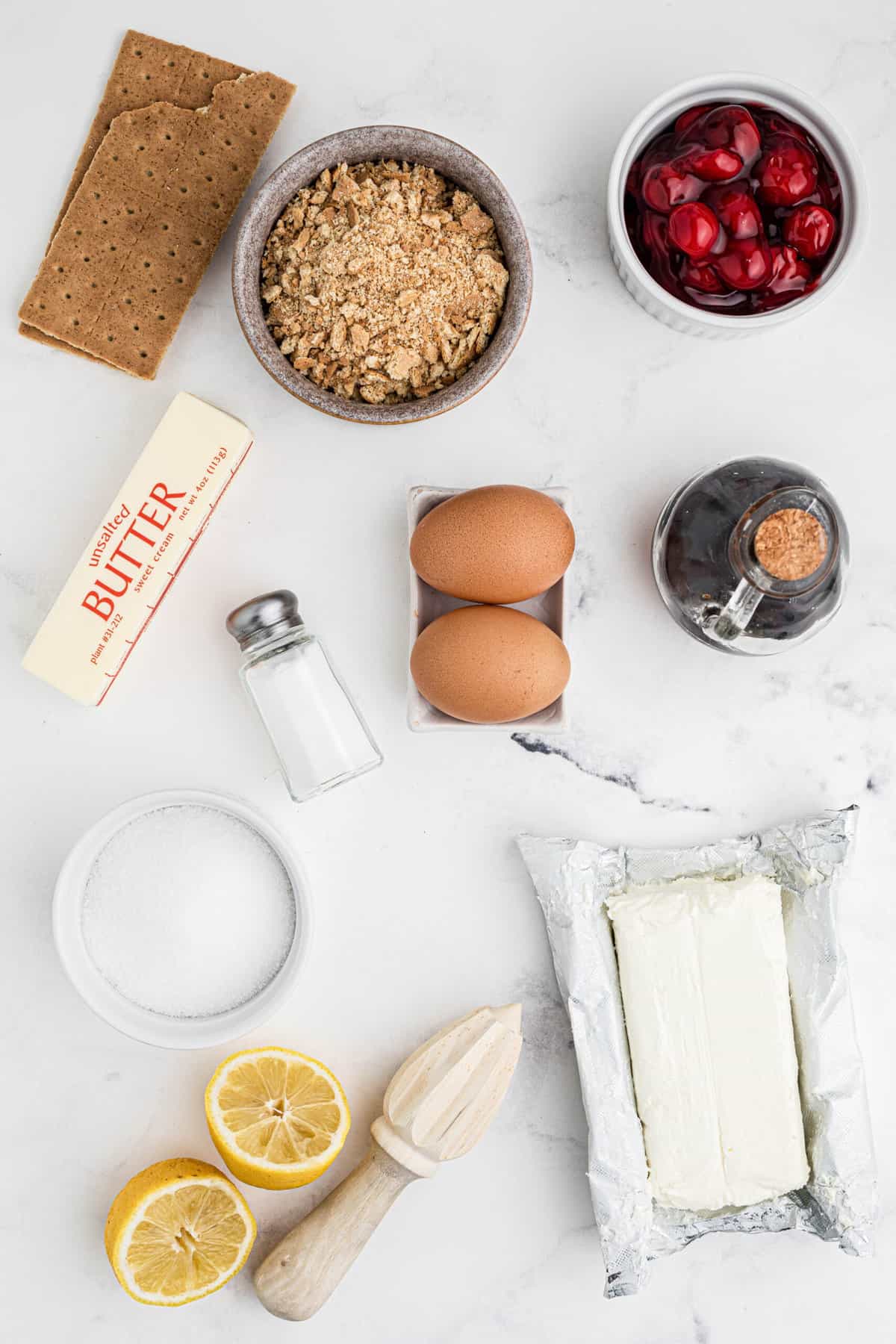 The ingredients for mini cherry cheesecakes are placed on a white surface. 