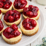 Several mini cherry cheesecakes are placed on a round white plate.