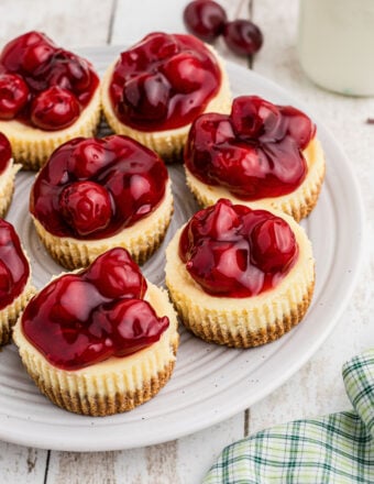 Several mini cherry cheesecakes are placed on a round white plate.