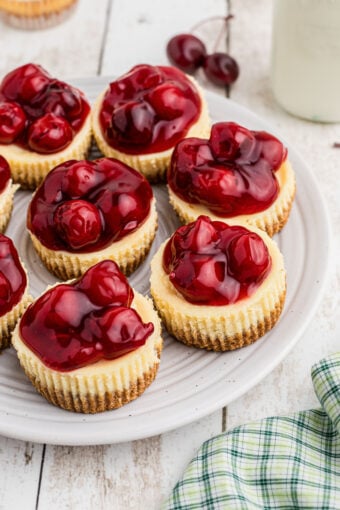 Several mini cherry cheesecakes are placed on a round white plate.