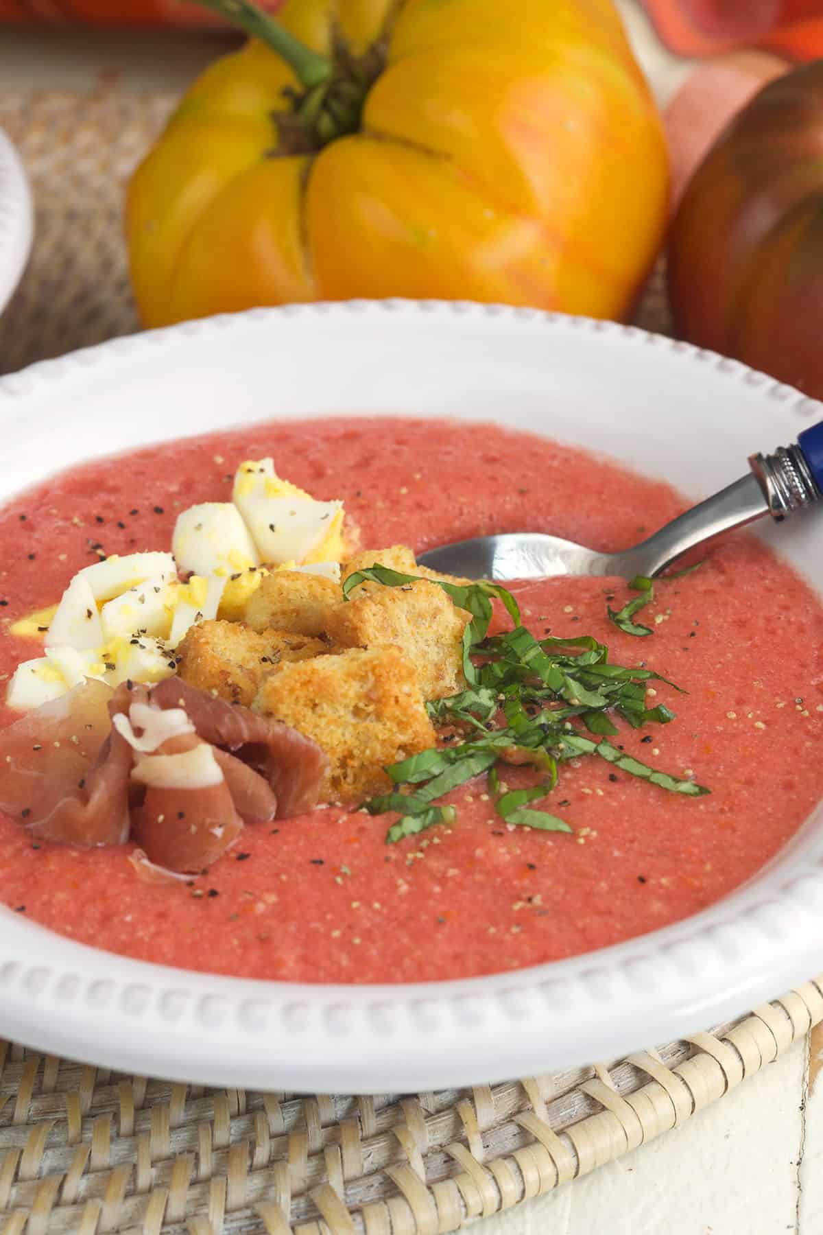 A bowl of salmorejo is garnished with croutons, ham, and herbs. 