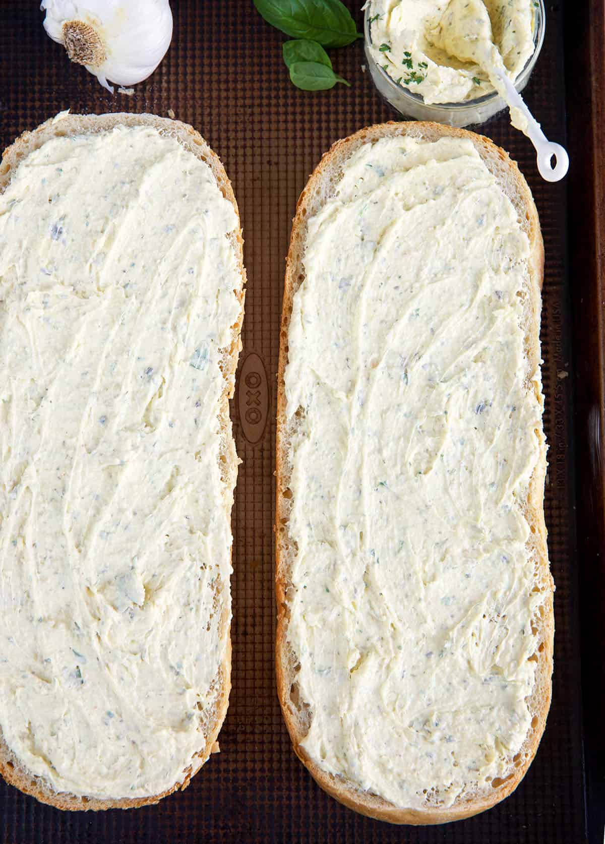Two halves of a baguette are smeared with garlic butter spread. 
