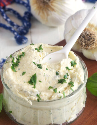 A small glass jar of garlic bread spread is garnishes with fresh herbs.