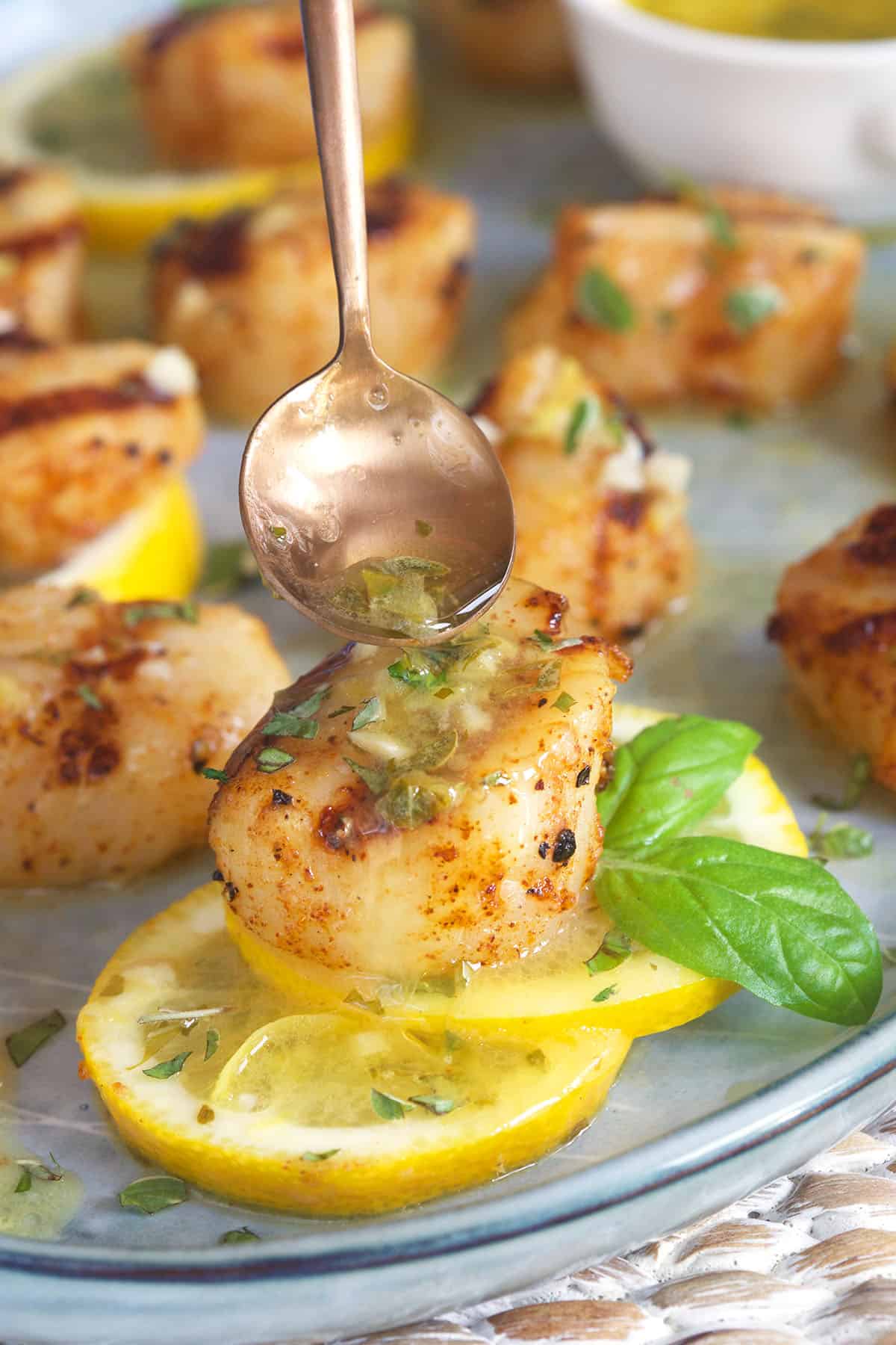 A single grilled scallop is being topped with melted butter sauce. 