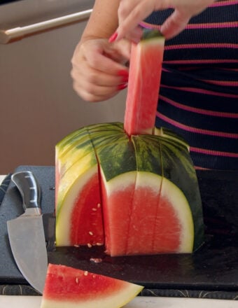 A stick of watermelon is being lifted from the cut melon.