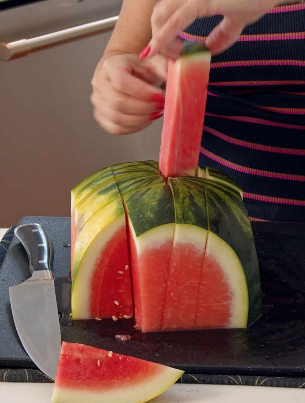 A stick of watermelon is being lifted from the cut melon. 