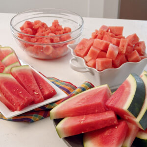 Slices of watermelon are placed in front of two bowls of watermelon chunks.