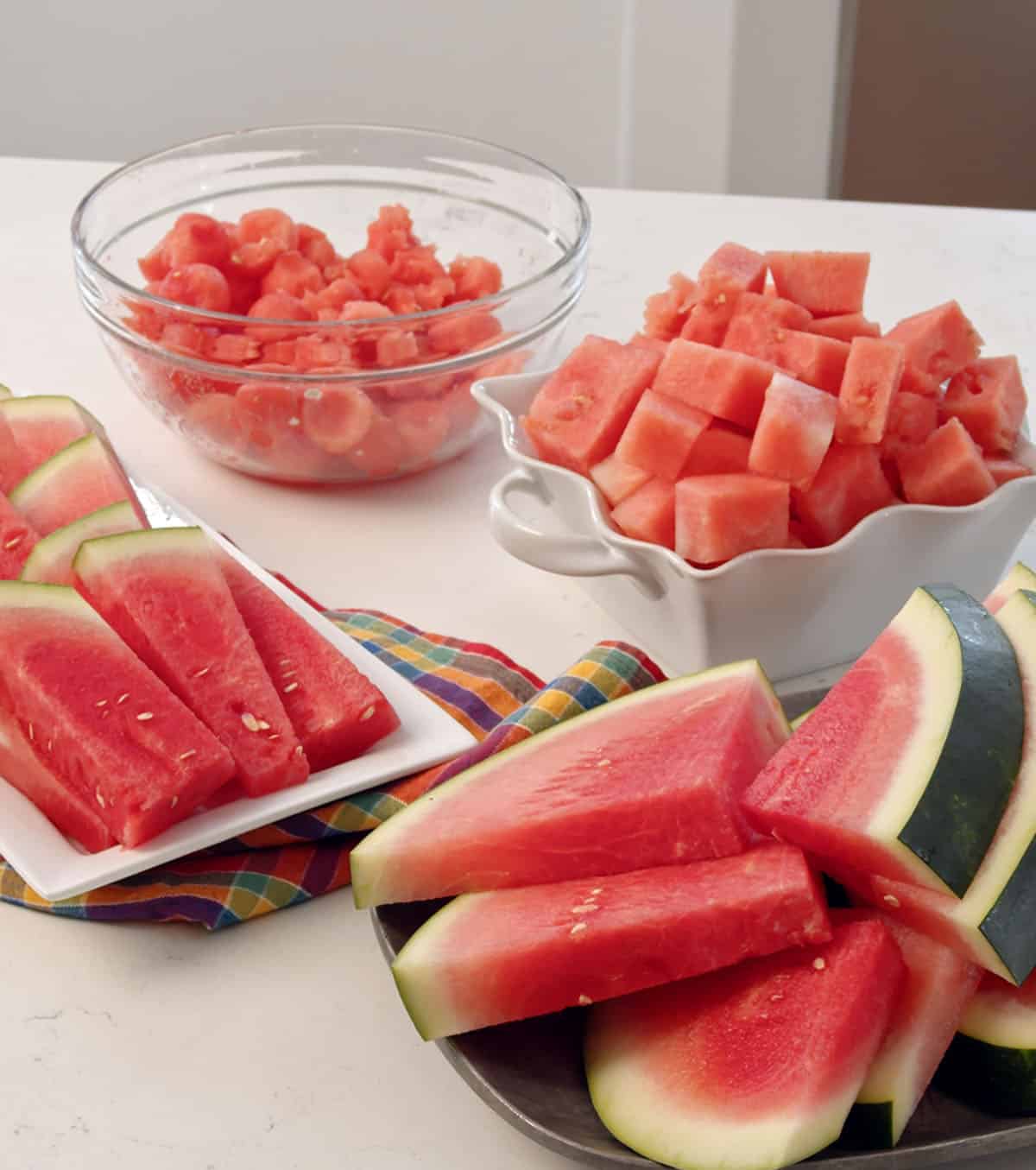 Slices of watermelon are placed in front of two bowls of watermelon chunks. 