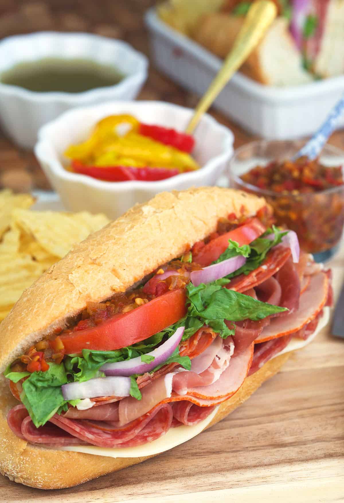 A small bowl of pickled peppers is placed behind a hoagie. 