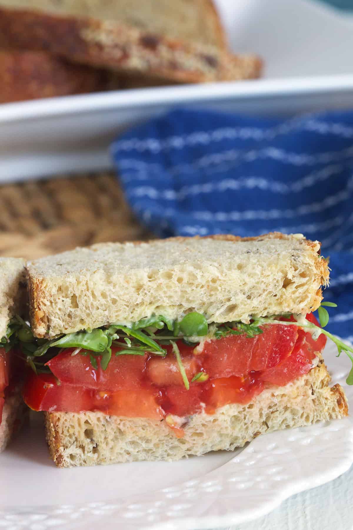 Half of a tomato sandwich is placed on a white plate. 
