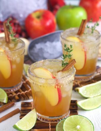 Three apple cider margaritas are placed next to sliced limes.