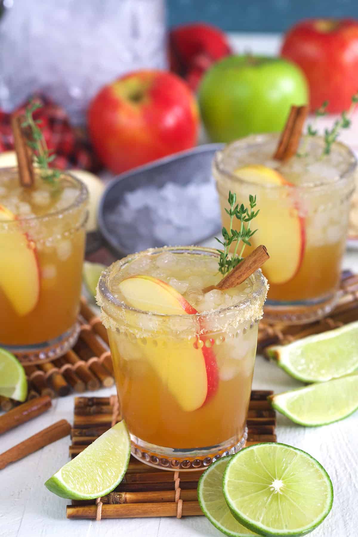 Three apple cider margaritas are placed next to sliced limes. 