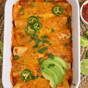 A baking dish is filled with cooked beef enchiladas and is garnished with avocado and jalapenos.