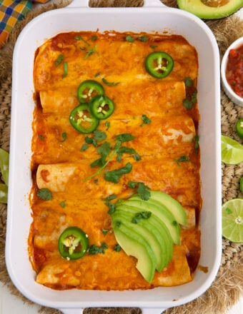 A baking dish is filled with cooked beef enchiladas and is garnished with avocado and jalapenos.