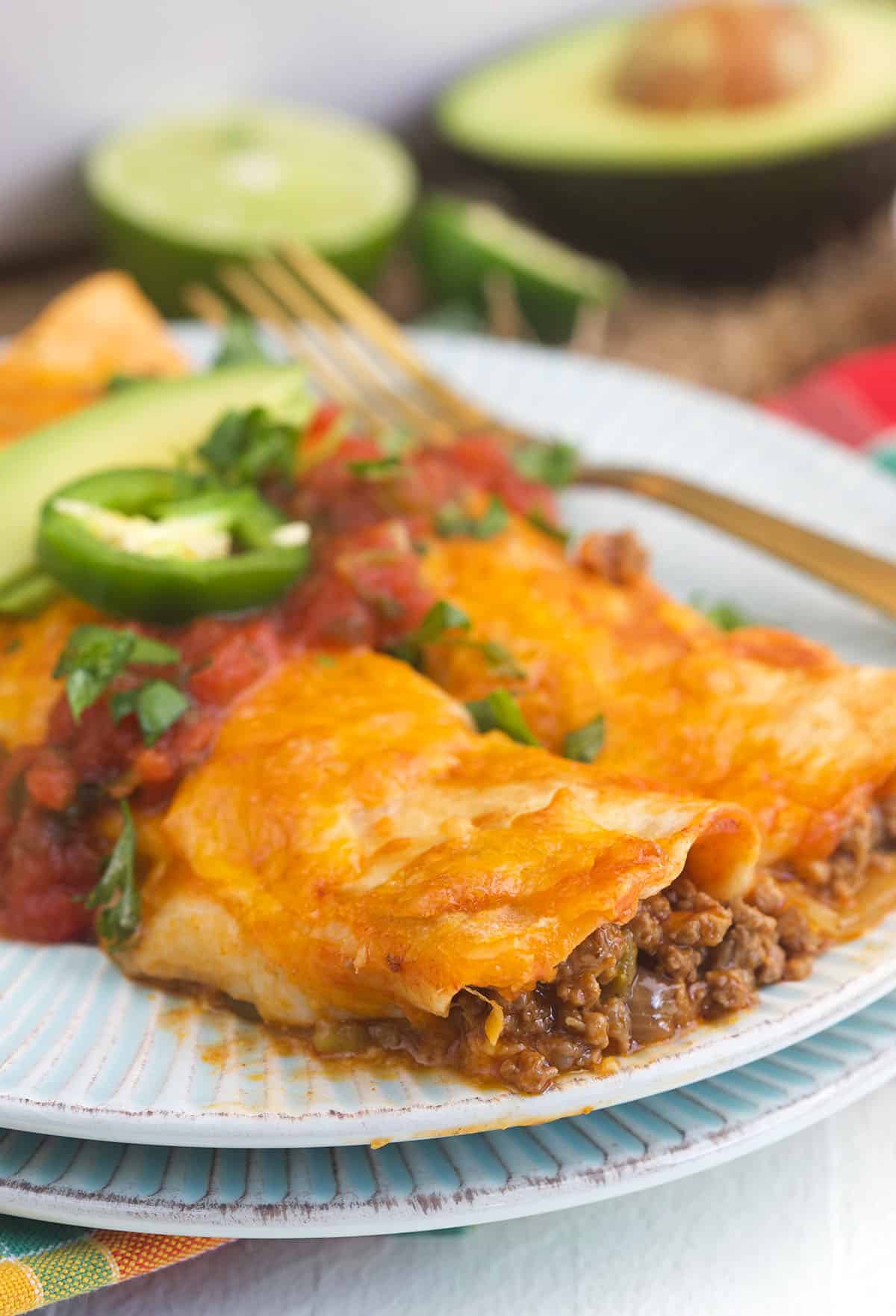 Garnished beef enchiladas are placed on a white plate. 