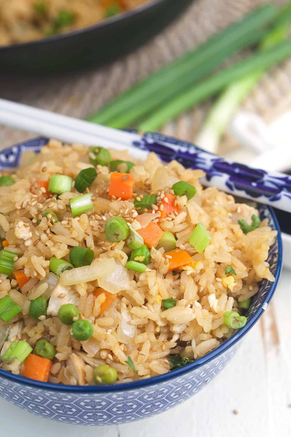 Chopsticks are placed on the edge of a bowl filled with chicken fried rice. 