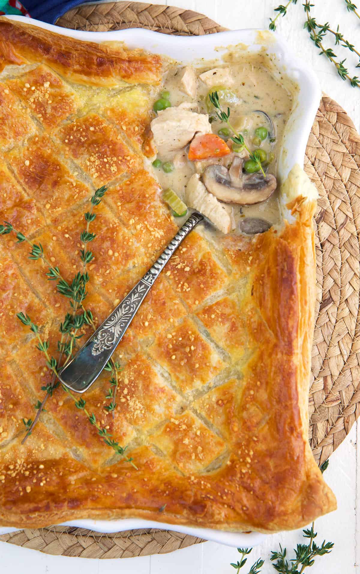 A serving spoon is placed in a baking dish filled with chicken pot pie casserole. 