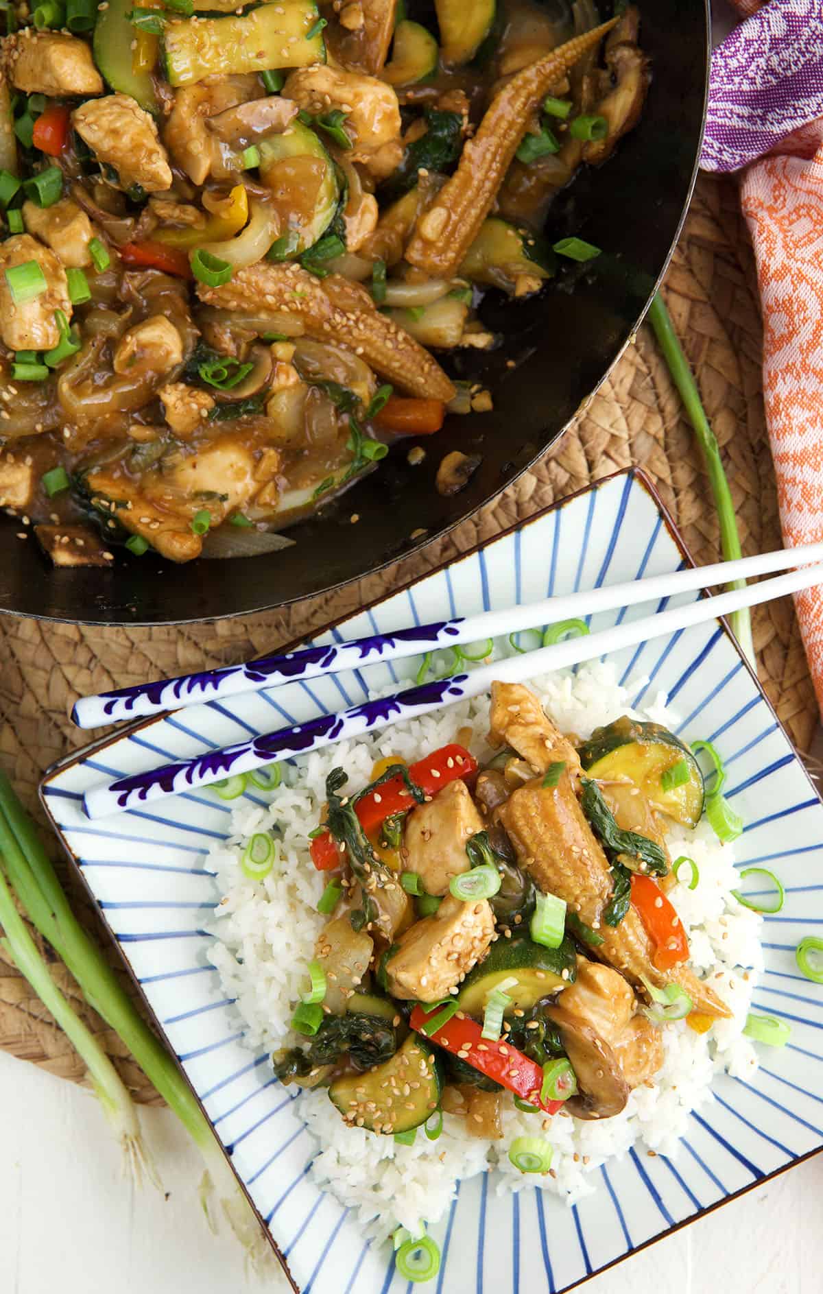 Chopsticks are placed on a plate with chicken stir fry and rice. 