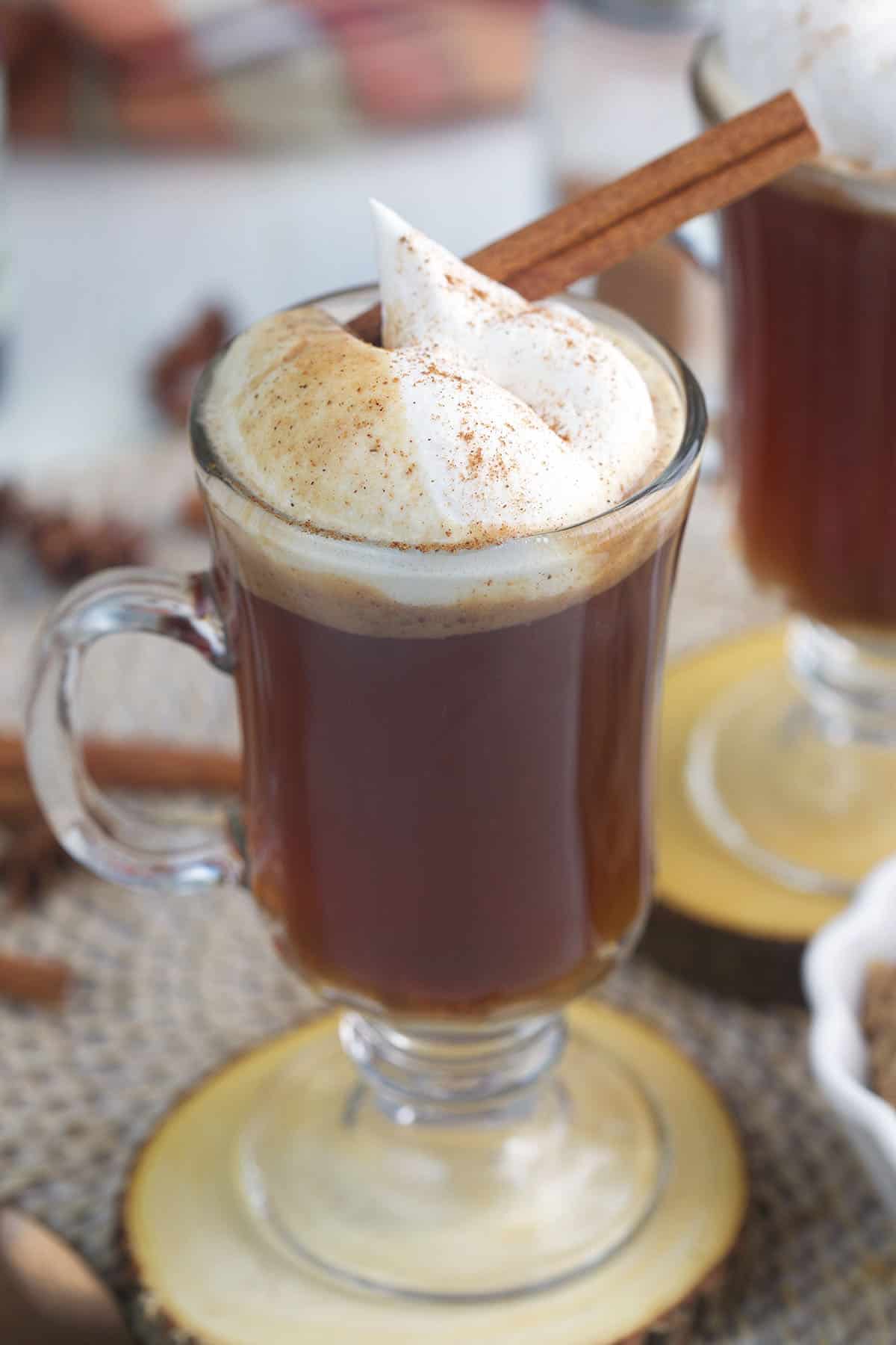 Whipped cream and a cinnamon stick garnish a glass mug of hot buttered rum.