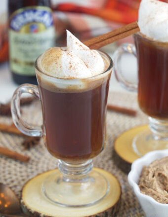 A cinnamon stick and whipped cream top a glass mug filled with hot buttered rum.