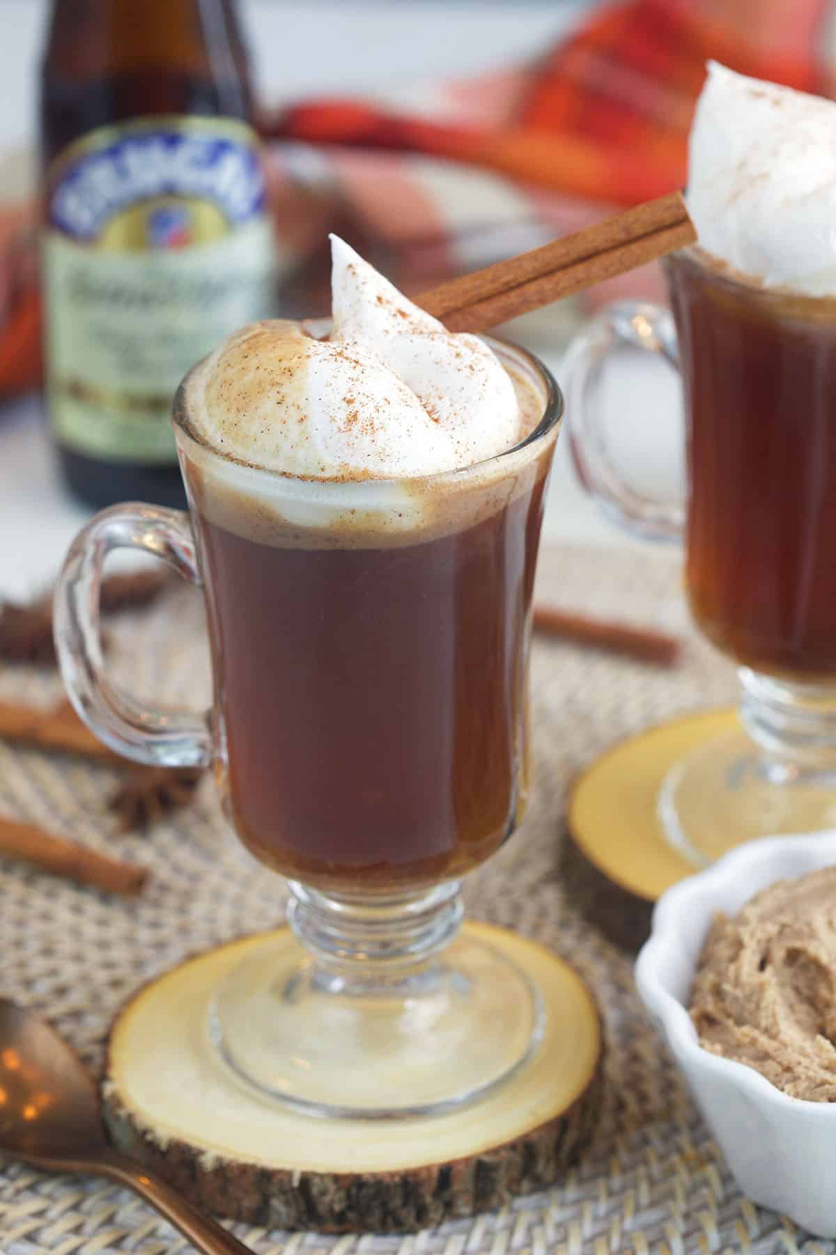 A cinnamon stick and whipped cream top a glass mug filled with hot buttered rum. 