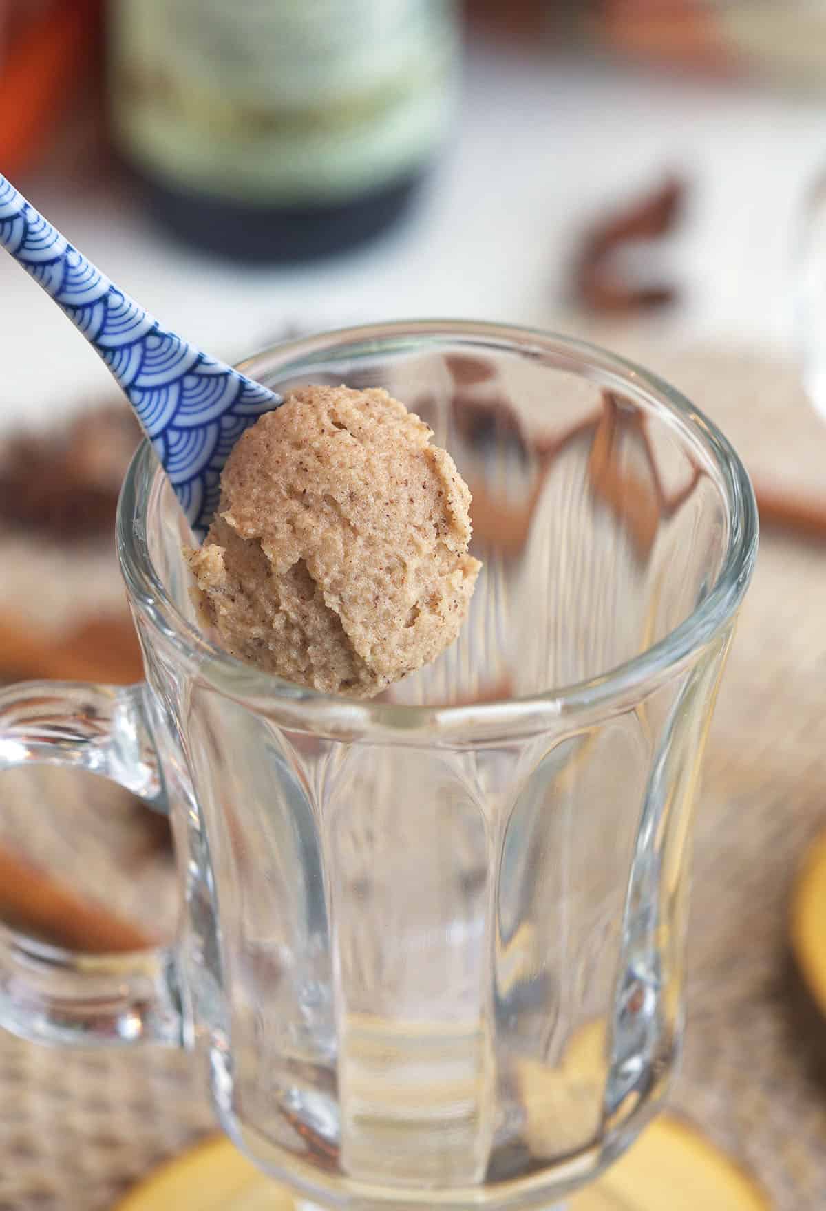 A spoonful of spiced butter is held above a glass mug.