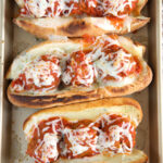 Three meatball subs are placed on a baking sheet.
