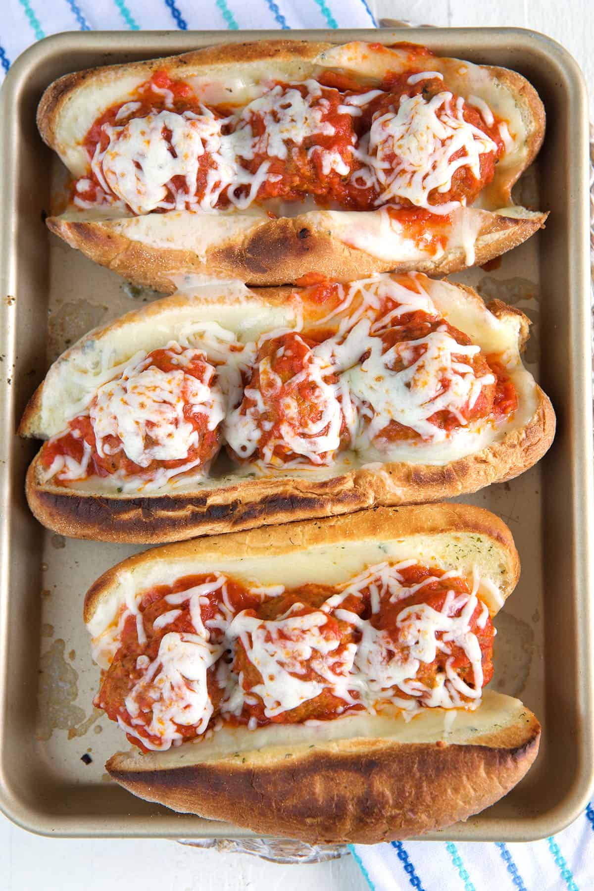 Three meatball subs are placed on a baking sheet. 