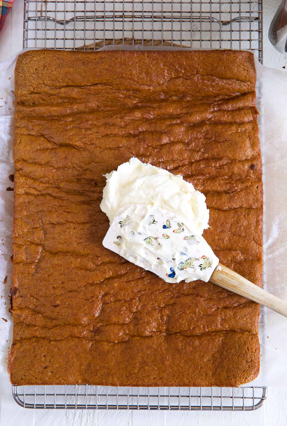 Cream cheese is being spread all over a sheet of pumpkin cake. 
