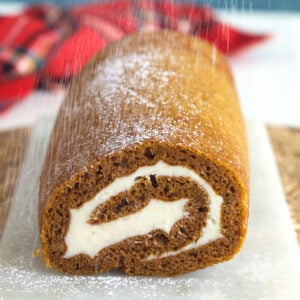 A pumpkin cake roll is being dusted with powdered sugar.