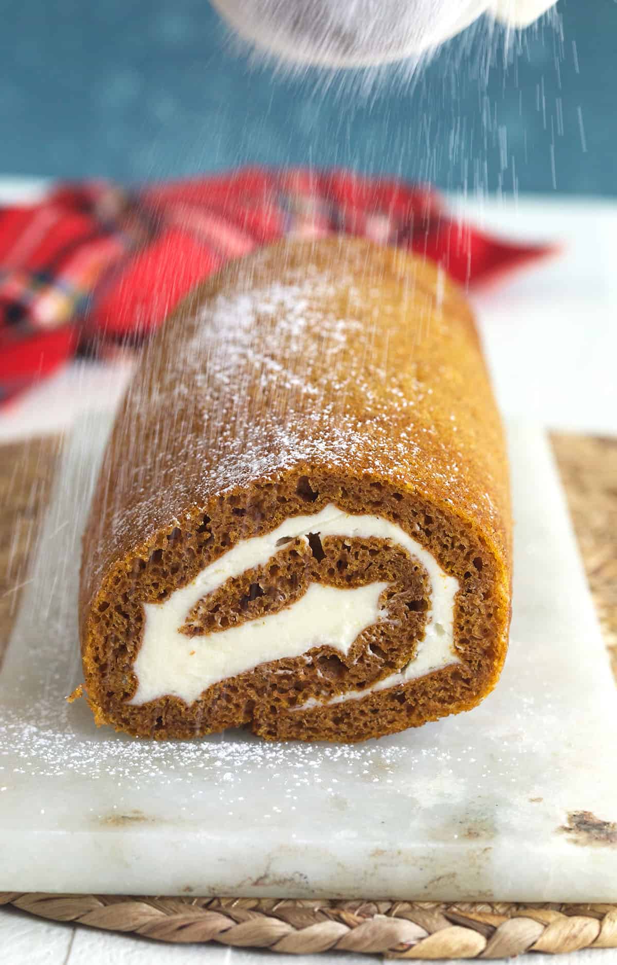A pumpkin cake roll is being dusted with powdered sugar. 