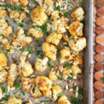 Roasted cauliflower is spread all over a baking sheet.