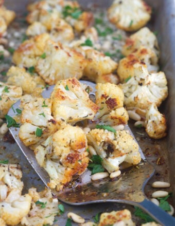 A spatula is lifting a serving of cauliflower from the baking sheet.